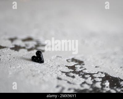 Schwarzes Herz auf Betonhintergrund, selektiver Fokus. Begriff von Morbidität, Trauer, Angst, unerwiderter Liebe, Zuneigung Stockfoto