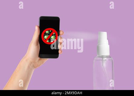 Säuberung mobiler Geräte während des Coronavirus-Ausbruchs. Antiseptisches Spray und Mann mit Smartphone auf lila Hintergrund, Nahaufnahme Stockfoto