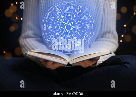 Junge Frau, die zu Hause Buch liest, und Darstellung eines Zodiakrades mit astrologischen Zeichen Stockfoto