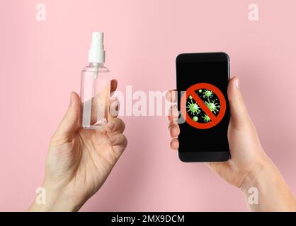 Säuberung mobiler Geräte während des Coronavirus-Ausbruchs. Frau mit Smartphone und antiseptischem Spray auf pinkfarbenem Hintergrund, Nahaufnahme Stockfoto