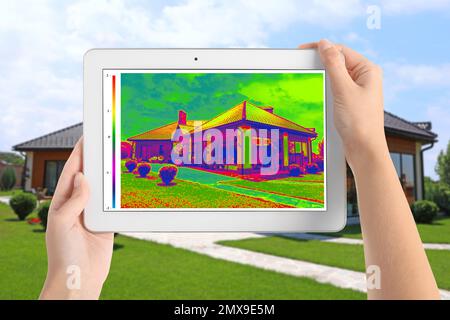 Frau erkennt Wärmeverlust im Haus mit einem Thermal-Viewer auf einem Tablet im Freien. Energieeffizienz Stockfoto