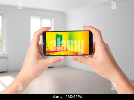 Frau, die einen Wärmeverlust im Raum mit dem Thermal-Viewer auf dem Smartphone erkennt. Energieeffizienz Stockfoto