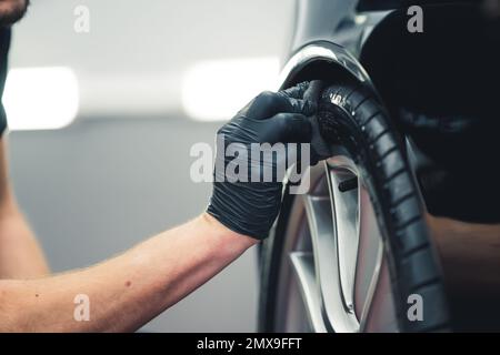 Schwärzung der Reifen. Ein unbekannter Mann, der einen Reifen mit einem Schwamm schwärzt. Professionelle Autoverbesserung in einer Garage. Hochwertiges Foto Stockfoto