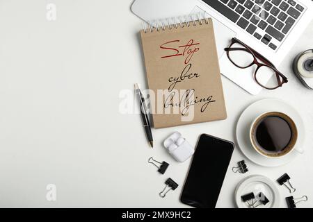 Notizbuch mit Phrase STOPPT CYBER-MOBBING, Laptop und Tasse Kaffee auf weißem Tisch, flach liegend. Platz für Text Stockfoto