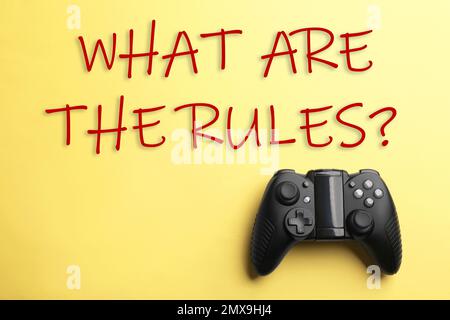 Moderner Videospiel-Controller mit Text WIE LAUTEN DIE REGELN auf gelbem Hintergrund, Draufsicht Stockfoto