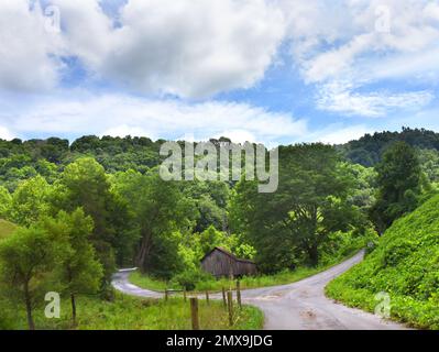 Schmale Landgabeln vor einer rustikalen, hölzernen Scheune. Die Straße führt durch die Appalachen. Stockfoto