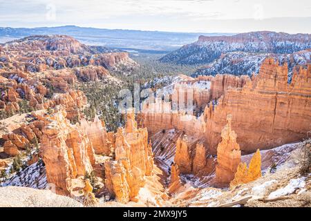 Der Bryce Canyon ist mit frisch gefallenem Schnee und fernen Bergen und leuchtend farbigen orangefarbenen Klippen geschmückt. Stockfoto