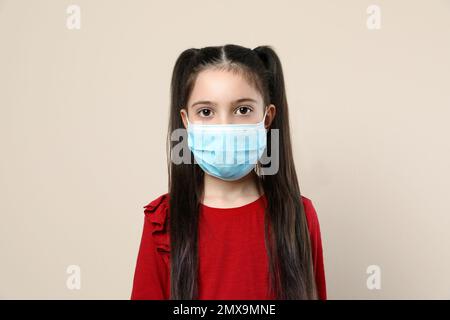 Kleines Mädchen mit medizinischer Maske auf beigefarbenem Hintergrund. Virenschutz Stockfoto