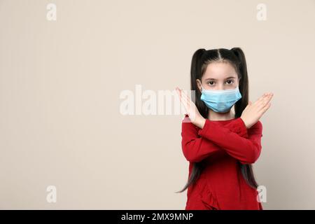 Kleines Mädchen mit medizinischer Maske auf beigefarbenem Hintergrund, Platz für Text. Virenschutz Stockfoto