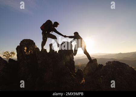 Silhouetten von zwei Menschen, die auf den Berg klettern und helfen. Hilfe- und Hilfekonzept. Stockfoto