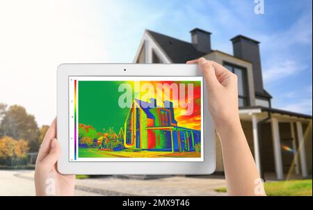 Frau erkennt Wärmeverlust im Haus mit einem Thermal-Viewer auf einem Tablet im Freien. Energieeffizienz Stockfoto