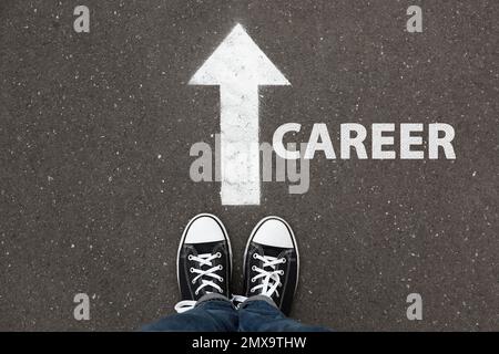 Eine Frau, die neben einem Pfeil auf Asphalt steht, Draufsicht. Career-Choice-Konzept Stockfoto