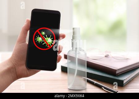 Säuberung mobiler Geräte während des Coronavirus-Ausbruchs. Antiseptisches Spray und Frau mit Smartphone in Innenräumen, Nahaufnahme Stockfoto