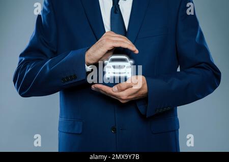 Ein Mann, der ein Bild von Auto auf grauem Hintergrund vorführt, Nahaufnahme. Autoversicherung Stockfoto