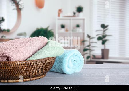 Korb aus Korb mit sauberen weichen Handtüchern auf grauem Holztisch im Badezimmer. Platz für Text Stockfoto