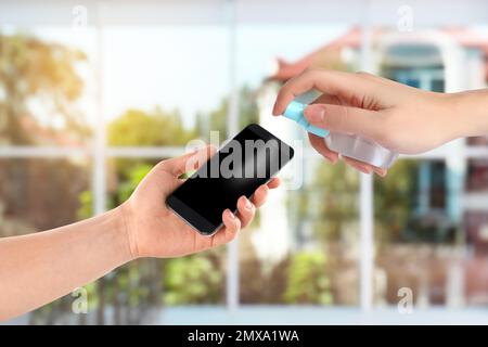 Frau desinfiziert Smartphone mit antiseptischem Spray in Innenräumen, Nahaufnahme. Sicherheit während des Coronavirus-Ausbruchs Stockfoto