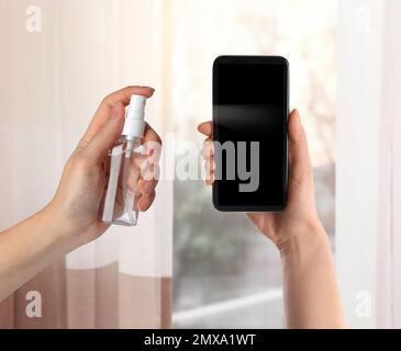 Frau desinfiziert Smartphone mit antiseptischem Spray in Innenräumen, Nahaufnahme. Sicherheit während des Coronavirus-Ausbruchs Stockfoto