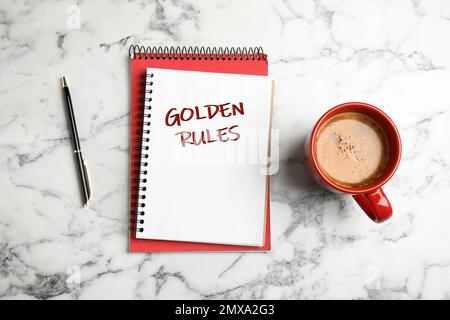 Flaches Notizbuch mit GOLDENEN REGELN und Kaffee auf weißem Marmorhintergrund Stockfoto