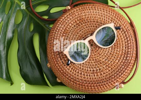 Bambustasche und Sonnenbrille mit Spiegelung von Palmen auf grünem Hintergrund, flach liegend Stockfoto