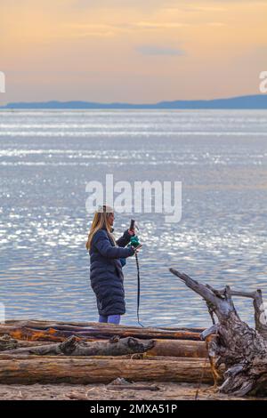 Blonde Frau, die am Strand in Steveston, British Columbia, Kanada, telefoniert Stockfoto