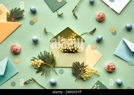 Ostern-Hintergrund. Mimosa- und Freesia-Blumen, Wachteleier, mintgrüne Umschläge und Farbpapier auf grünem Hintergrund. Flach liegend, über Kopf, knurrt Stockfoto
