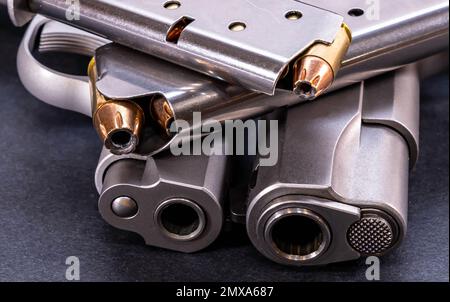 Zwei 1911-Pistolen aus Edelstahl, eine 45 ACP und die andere ein Kaliber 380 mit einem beladenen Magazin auf jeder Oberseite auf schwarzem Hintergrund Stockfoto