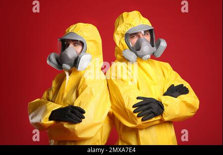 Mann und Frau tragen chemische Schutzanzüge auf rotem Hintergrund. Virusforschung Stockfoto