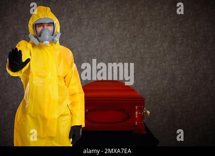 Beerdigung während der Coronavirus-Pandemie. Mann im Schutzanzug in der Nähe von Sarg im Haus Stockfoto