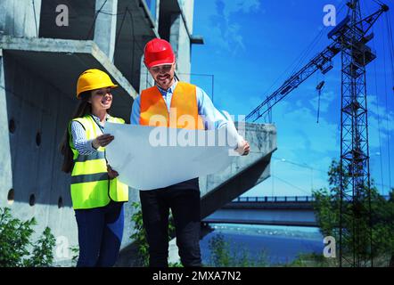Professionelle Ingenieure in der Sicherheitsausrüstung mit Zeichnungsarbeiten auf der Baustelle Stockfoto