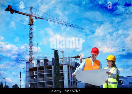 Professionelle Ingenieure in der Sicherheitsausrüstung mit Zeichnungsarbeiten auf der Baustelle Stockfoto