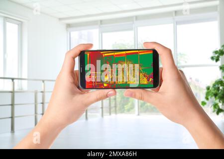 Frau, die einen Wärmeverlust im Raum mit dem Thermal-Viewer auf dem Smartphone erkennt. Energieeffizienz Stockfoto