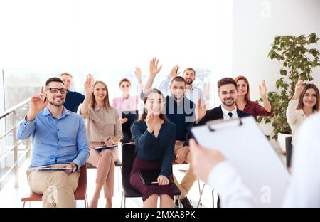 Menschen, die sich bei Geschäftsschulungen in geschlossenen Räumen die Hand heben, um Fragen zu stellen Stockfoto