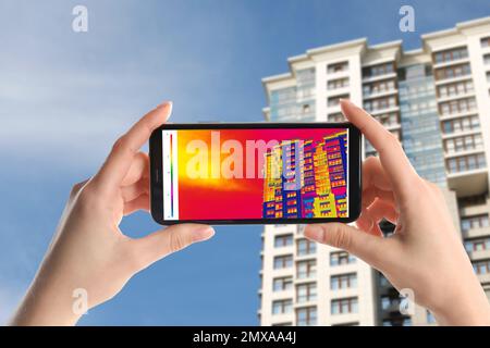 Frau erkennt Wärmeverlust im Gebäude mit dem Thermal-Viewer auf dem Smartphone im Freien. Energieeffizienz Stockfoto