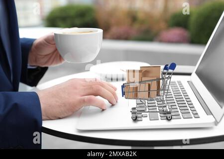 Mann, der online mit einem Laptop einkauft, kleiner Wagen mit Kisten auf dem Computer Stockfoto