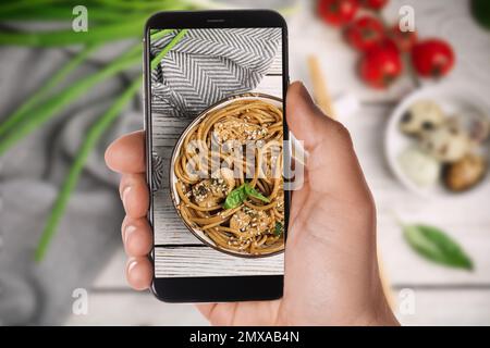 Blogger macht ein Foto von köstlichen Buchweizennudeln mit Fleisch am Tisch, Nahaufnahme. Lebensmittelfotografie Stockfoto