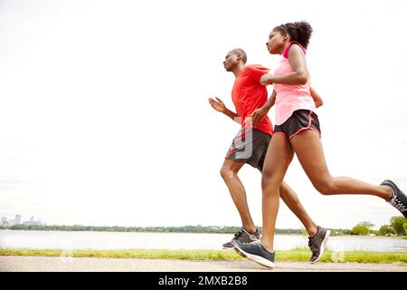 Ruhiges Joggen. Durchgehende Seitenansicht von zwei Athleten, die neben einem See laufen. Stockfoto