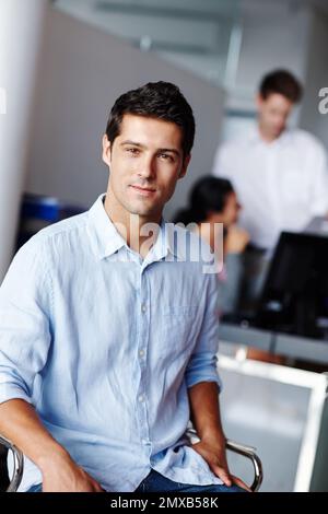 Er hat das Erlebnis, das man sich wünscht. Ein selbstbewusster junger Geschäftsmann mit seinen Kollegen verschwommen im Hintergrund. Stockfoto