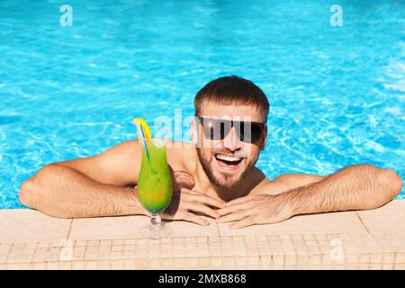 Junger bärtiger Mann mit erfrischendem Cocktail im Swimmingpool des Resorts Stockfoto