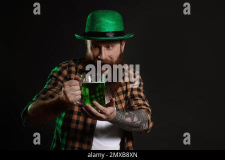 Bärtiger Mann mit grünem Bier auf schwarzem Hintergrund. St. Patrick's Day-Feier Stockfoto