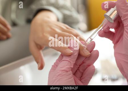 Professionelle Maniküre gießt Öl auf die Nägel des Kunden im Schönheitssalon, Nahaufnahme Stockfoto