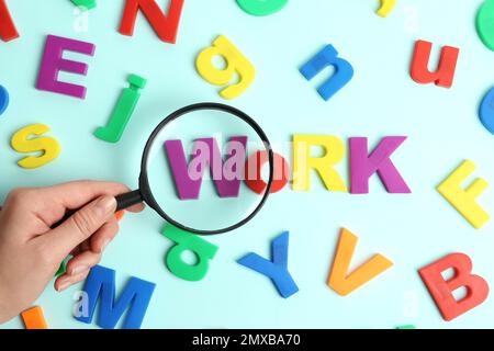 Frau, die eine Lupe über WORTSCHRIFTEN hält, die mit Magnetbuchstaben auf hellblauem Hintergrund gemacht wurden, Draufsicht. Suchkonzept Stockfoto