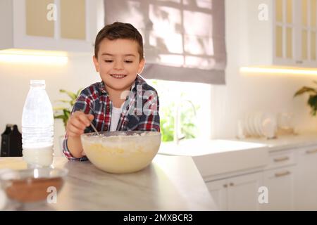 Süßer kleiner Junge, der zu Hause in der Küche Teig kocht Stockfoto