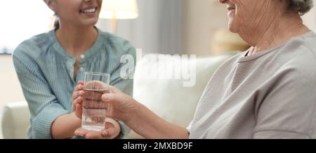 Junge Frau, die einer älteren Dame drinnen Wasser gibt, Bannerdesign. Seniorenfürsorge Stockfoto