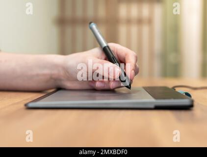 Handgehaltener Eingabestift, mit dem auf einem digitalen Tablet auf einem Holzschreibtisch gezeichnet wird. Illustrator, Designer bei der Arbeit. Hochwertiges Foto Stockfoto