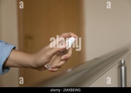 Frau, die Antiseptikum auf Metallgeländer spritzt, drinnen, Nahaufnahme Stockfoto