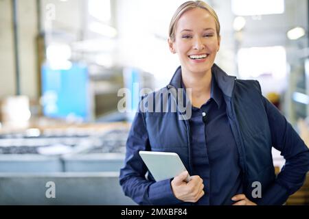Verantwortlich in der Fabrik. Porträt eines lächelnden Managers, der ein digitales Tablet hält, während er in der Fabrik steht. Stockfoto