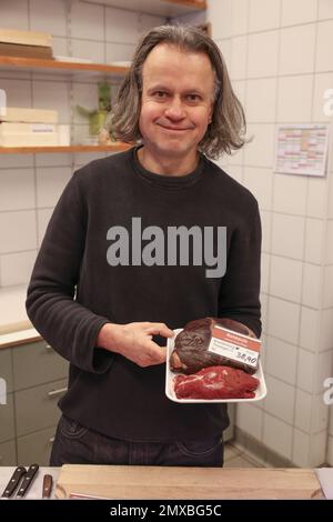 Berlin, Deutschland. 27. Januar 2023. Lutz Albrecht aus dem Wild & Geflügel Albrecht Metzger Store steht in seinem Laden mit einem Bein Wild. Die Preise für Rotwild und Wildschweine sind in jüngster Zeit stark gestiegen, doch ist Wild gefragt. (Zu dpa „Sattel des Wildschweins und Bein des Wildschweins: Begehrt, aber selten“) Kredit: Joerg Carstensen/dpa/Alamy Live News Stockfoto