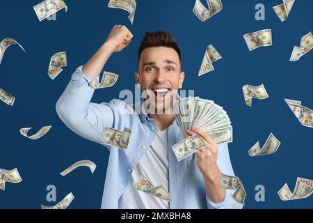 Mann mit amerikanischen Dollar unter Geld, Regen auf blauem Hintergrund Stockfoto