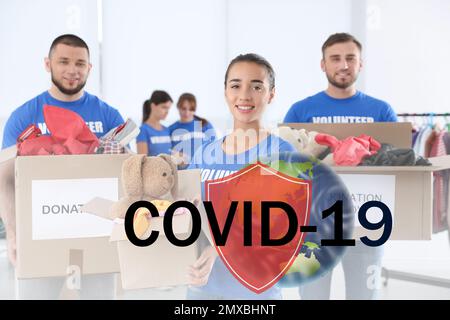 Freiwillige, die sich zusammengeschlossen haben, um während des COVID-19-Ausbruchs zu helfen. Gruppe von Menschen mit Spenden in Gebäuden, Schilde und Weltkugel Illustrationen Stockfoto