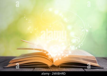 Symphonie mit musikalischen Noten aus einem offenen Buch auf einem Holztisch vor verschwommenem Hintergrund Stockfoto